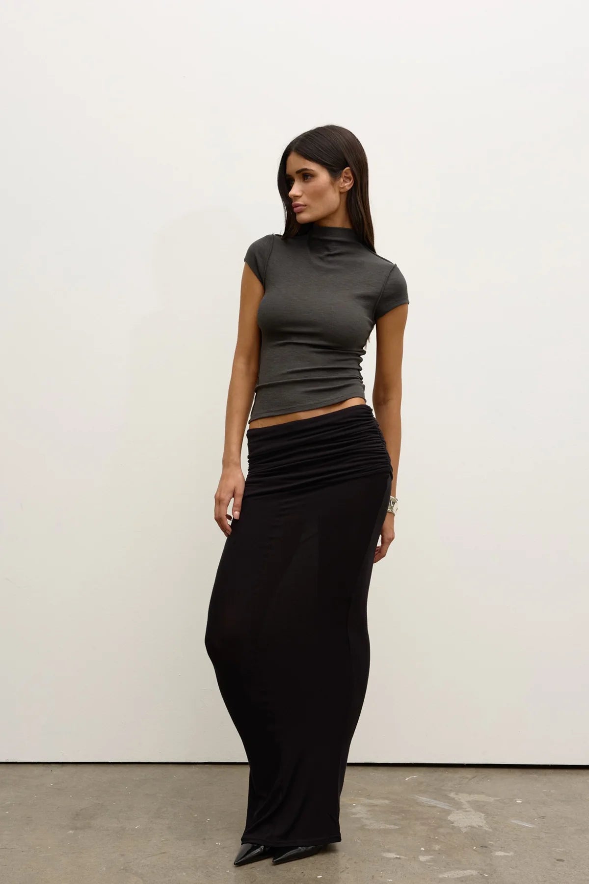 Woman wearing a gray top and black skirt against a white wall