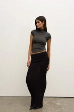 Woman wearing a gray top and black skirt against a white wall