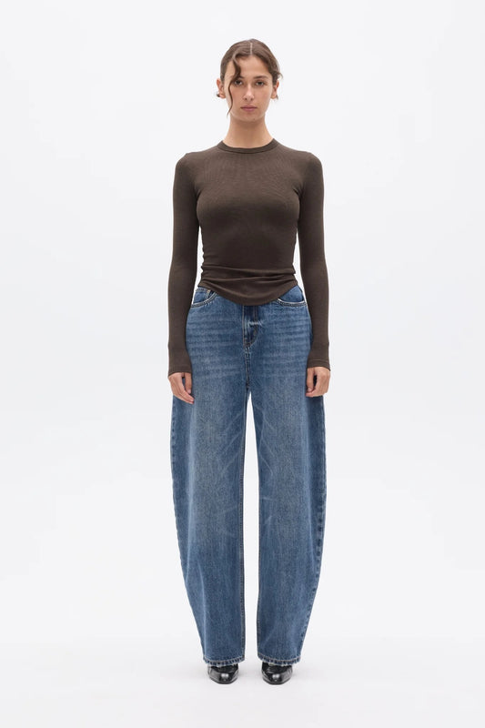 Model wearing an Espresso fitted long-sleeve top with blue barrel-leg jeans and black pointed shoes, showing the crew neckline, slim silhouette and curved front hem, front view