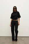 Model wearing a black relaxed-fit short-sleeve T-shirt with black straight-leg jeans, oversized sunglasses and black heels, showing the crew neckline and slightly cropped silhouette, front view