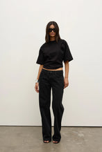 Model wearing a black relaxed-fit short-sleeve T-shirt with black straight-leg jeans, oversized sunglasses and black heels, showing the crew neckline and slightly cropped silhouette, front view