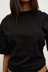 Close-up of the black short-sleeve T-shirt, showing the smooth fabric, crew neckline, dropped shoulders and relaxed fit