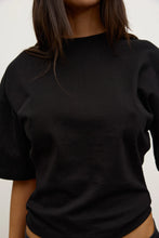 Close-up of the black short-sleeve T-shirt, showing the smooth fabric, crew neckline, dropped shoulders and relaxed fit