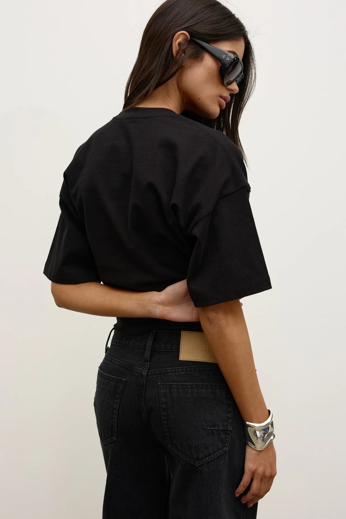 Model wearing the black short-sleeve T-shirt with black jeans, showing the dropped shoulders, loose sleeves and relaxed silhouette, back view