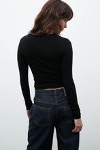 Person wearing a black long-sleeve top and dark jeans on a white background