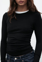 Person wearing a black long-sleeve top and blue jeans on a white background