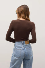 Person wearing a brown long-sleeve top and blue jeans on a plain background
