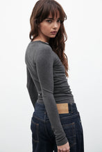 Woman wearing a gray long-sleeve top and dark jeans on a white background