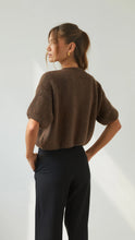 Woman wearing a brown sweater and black pants against a white background
