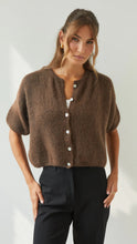 Woman wearing a brown cardigan with button details against a plain background
