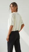 Back three-quarter view of the ivory cardigan highlighting its relaxed shape, short sleeves and ribbed hem.