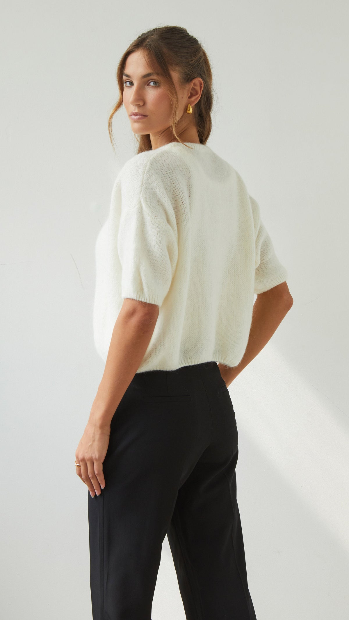 Back three-quarter view of the ivory cardigan highlighting its relaxed shape, short sleeves and ribbed hem.