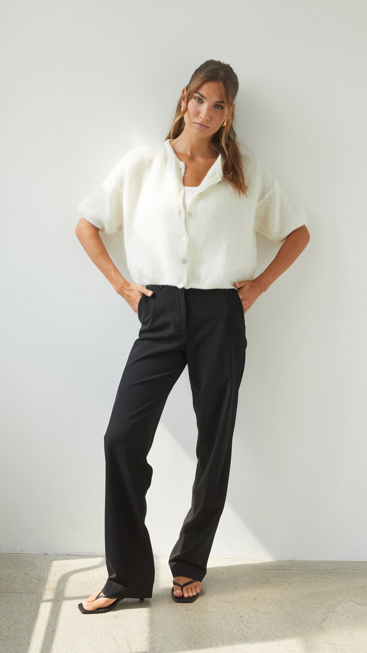 Full-length view of the ivory cardigan styled with black wide-leg trousers, showing its cropped length and short-sleeve design.