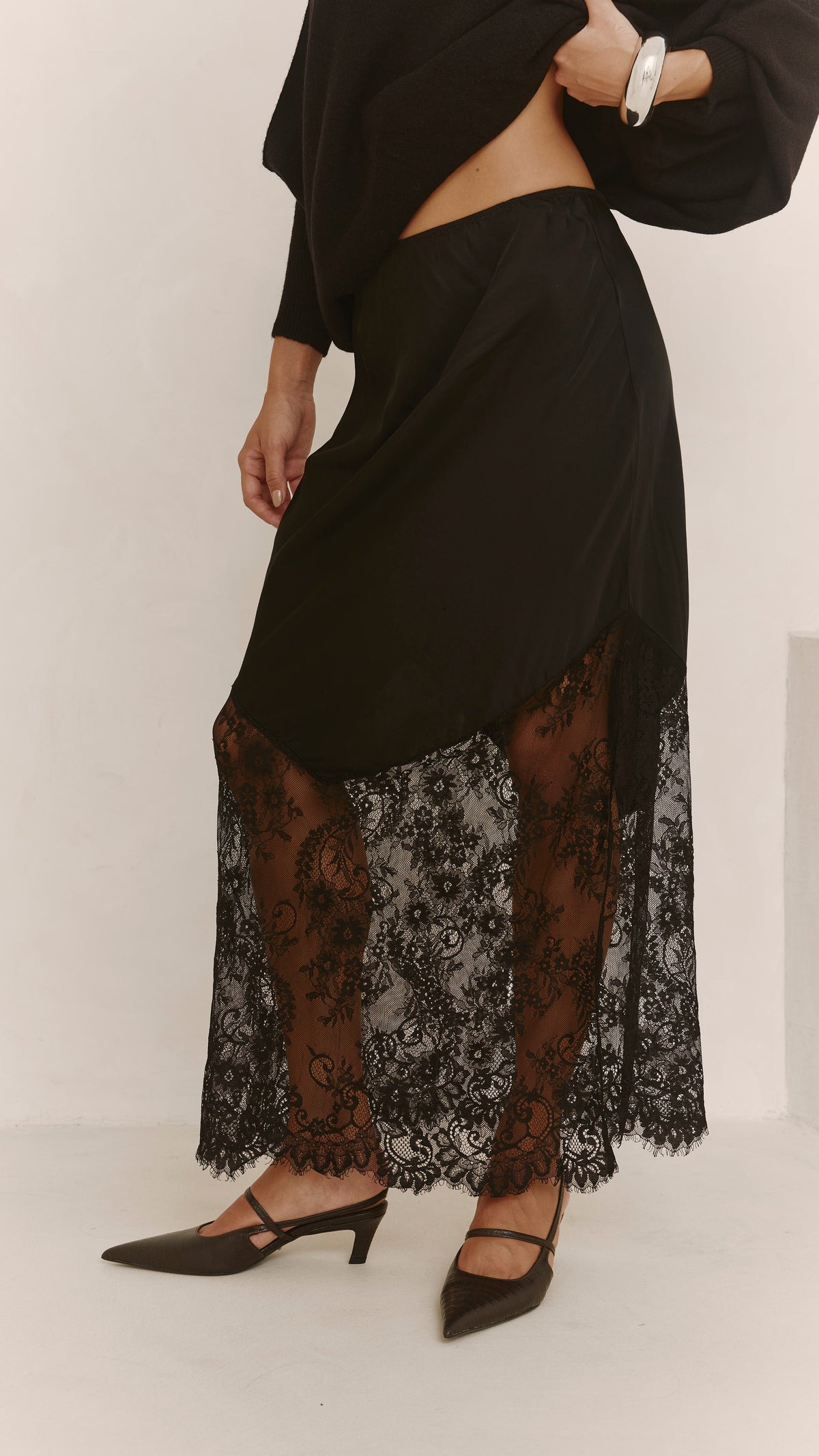 A close-up of the black skirt showing the draped satin overlay, elasticated waistband and sheer floral lace panels.