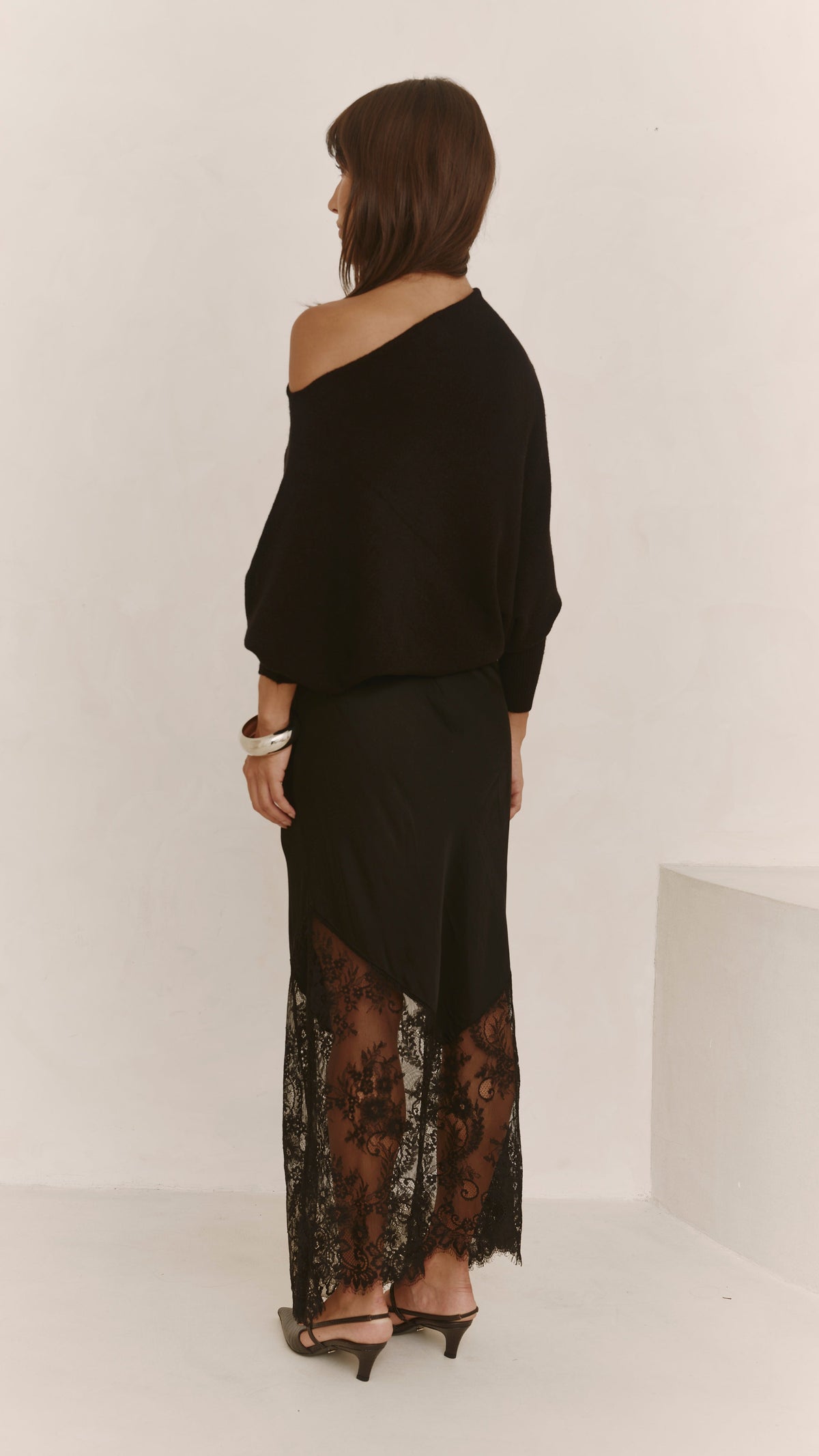 A back three-quarter view of the black lace skirt, highlighting the flowing silhouette and sheer lace hem.