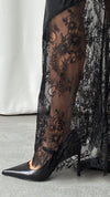 A close-up of the black skirt's sheer floral lace panels and scalloped edge styled over pointed-toe shoes.