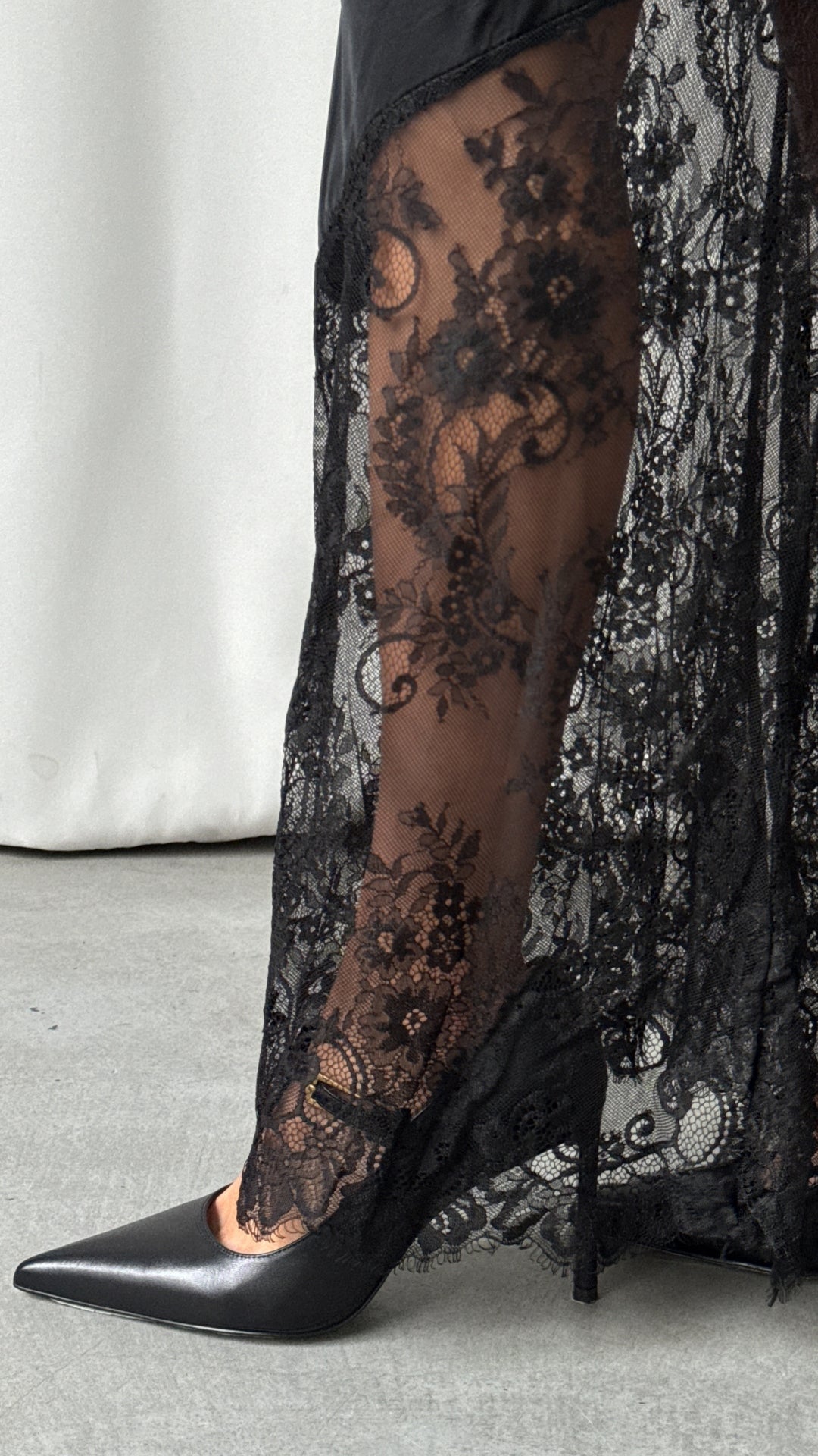 A close-up of the black skirt's sheer floral lace panels and scalloped edge styled over pointed-toe shoes.
