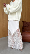 A model wearing the Moonbeam skirt with a cream knit jumper, highlighting the asymmetrical overlay and lace hem.