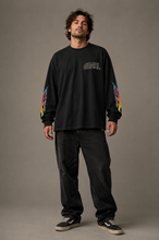 Full-length front view of a man wearing the oversized black long sleeve tee with washed black jeans and sneakers in a neutral studio setting.