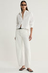 A model wearing a white cropped shirt with a collared neckline, open front buttons and long sleeves, styled with white trousers and black sandals in an angled front pose.