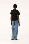 Model wearing the black Zoe Tee with light blue jeans, showing the simple back, relaxed shoulders and boxy silhouette, full-length back view