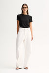 A model wearing a fitted black short-sleeve tee with a round neckline, tucked into white wide-leg trousers and paired with flat black sandals in a full-length front view.