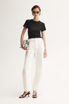 A model wearing a fitted black crew-neck tee and white wide-leg trousers, accessorised with dark sunglasses, a patterned clutch and black heeled sandals in a front-facing studio pose.