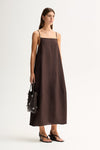 Three-quarter front view of a woman wearing a chocolate maxi dress with thin straps and a flowing relaxed shape.
