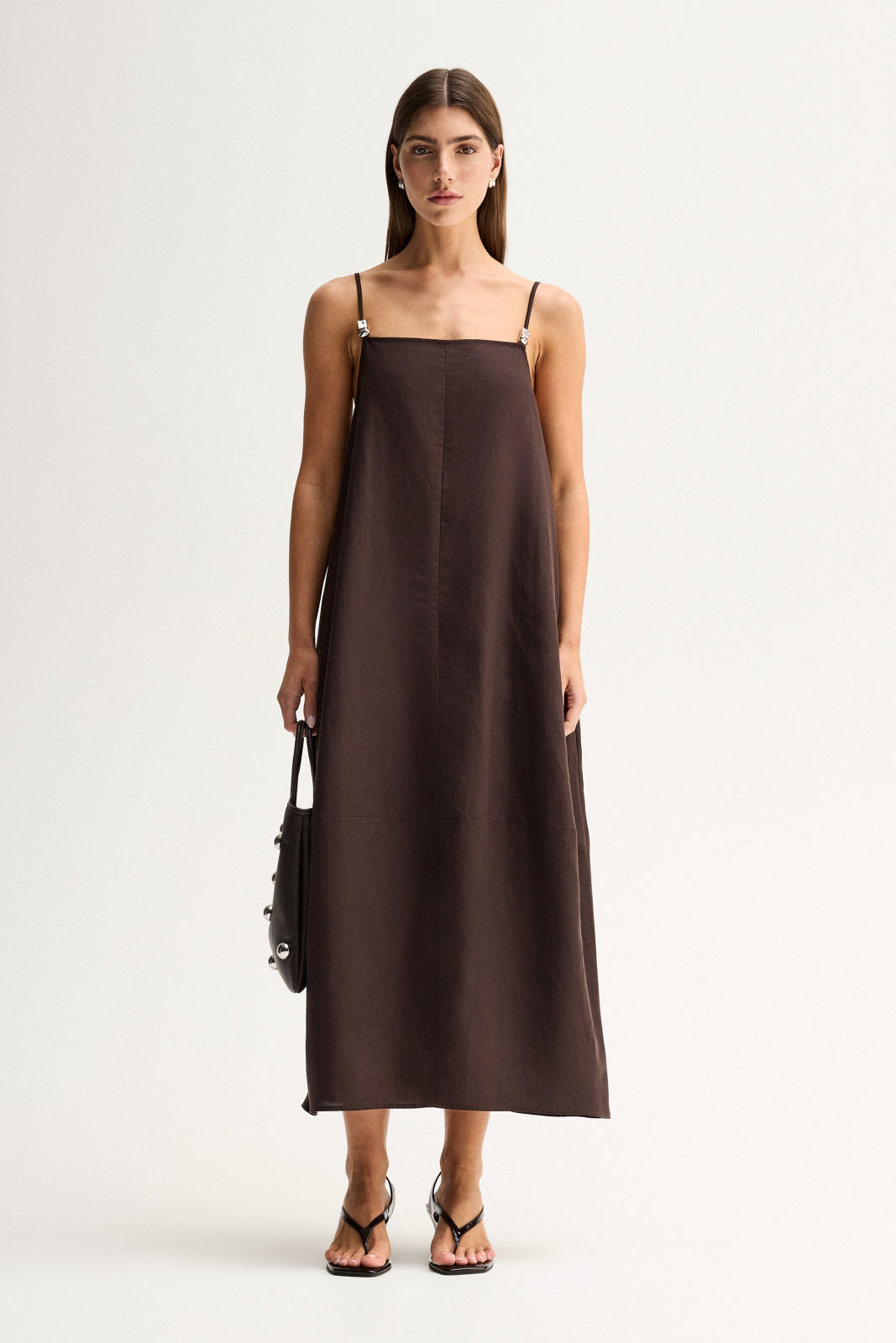 Front view of a woman wearing a chocolate maxi dress with a straight neckline, thin straps and a relaxed full-length silhouette.