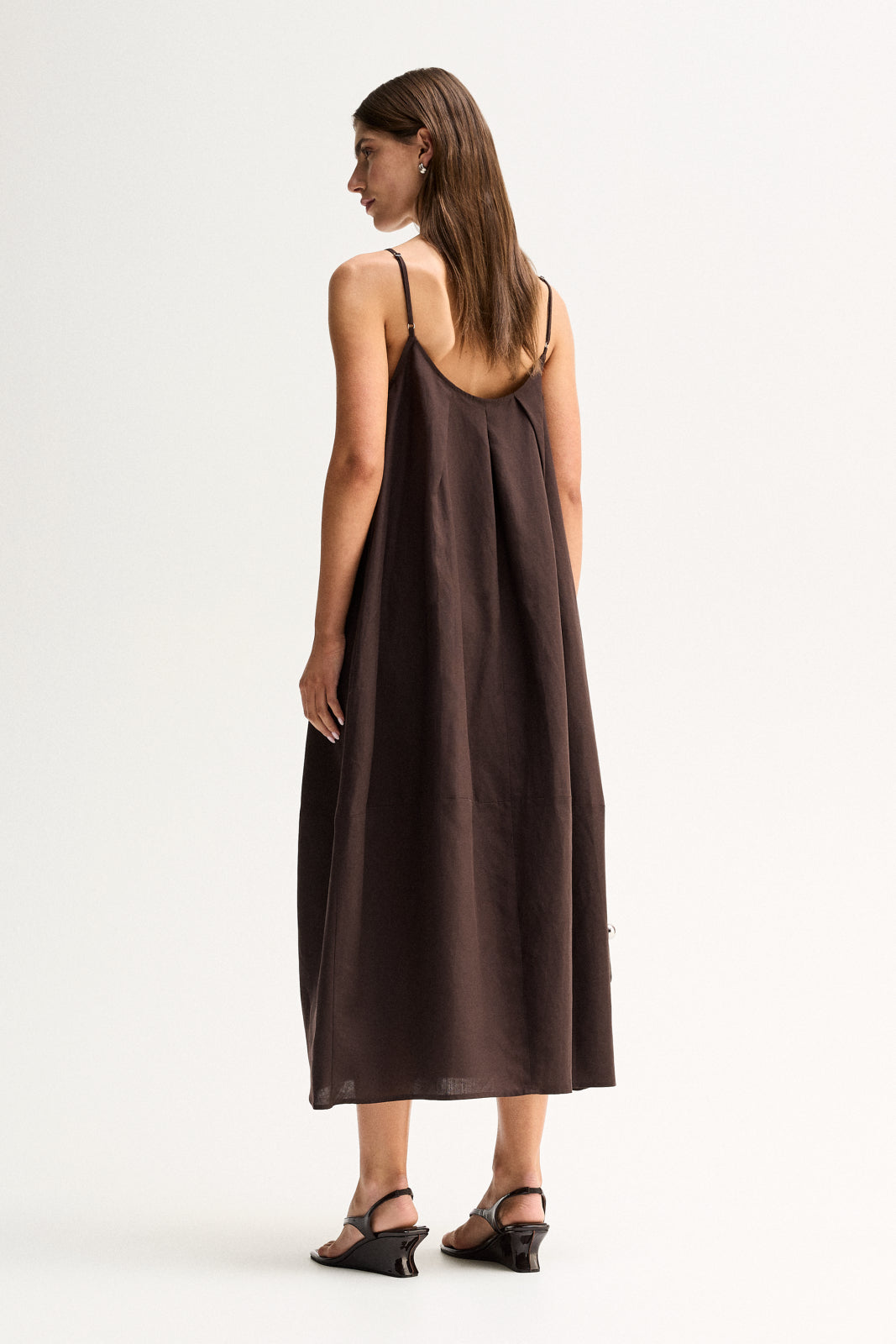 Back three-quarter view showing the chocolate maxi dress with thin straps and a relaxed flowing shape.