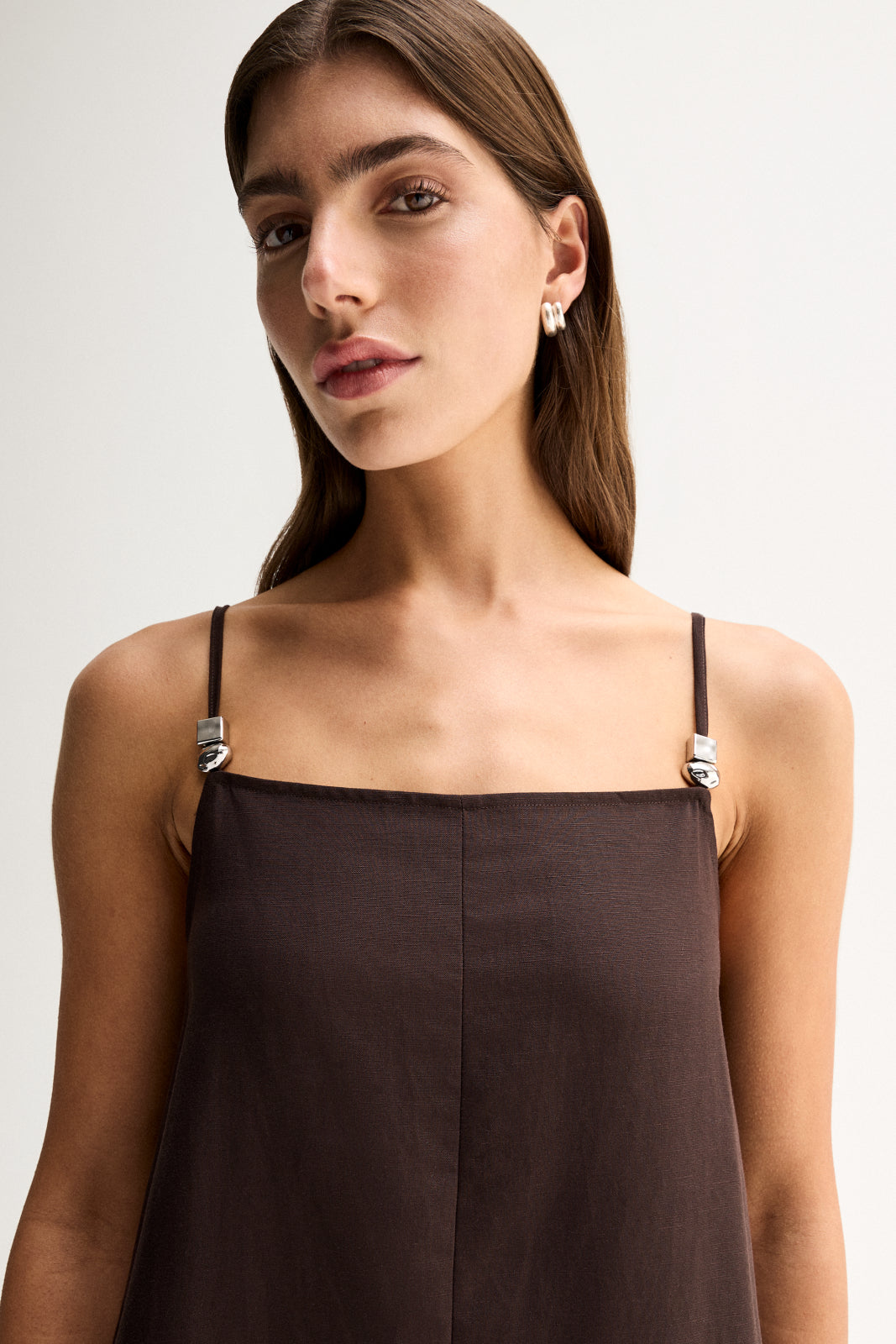Close-up of the chocolate dress showing the straight neckline, thin adjustable straps and silver hardware details.