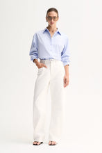 Model wearing the Light Blue Elka Collective Carter Shirt with white wide-leg jeans, black thong sandals and sunglasses, showing the relaxed oversized fit, spread collar and button-through front, full-length front view