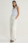 A model wearing a pale blue marled scoop-neck knit top and cream wide-leg trousers, photographed from an angled front view with one hand in a trouser pocket.