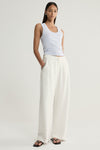 A model wearing a pale blue marled sleeveless top with a rounded scoop neckline and cream wide-leg trousers, standing with one hand in a pocket and a silver bracelet at the wrist.