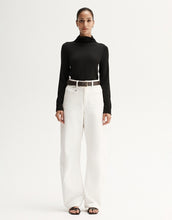 Model wearing a black fitted long-sleeve top with white wide-leg trousers and black sandals, front view