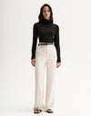 Model wearing a black fitted long-sleeve top with white wide-leg trousers and black sandals, full-length front view
