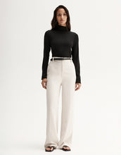 Model wearing a black fitted long-sleeve top with white wide-leg trousers and black sandals, full-length front view