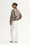 Person wearing a beige sweater and white pants on a white background