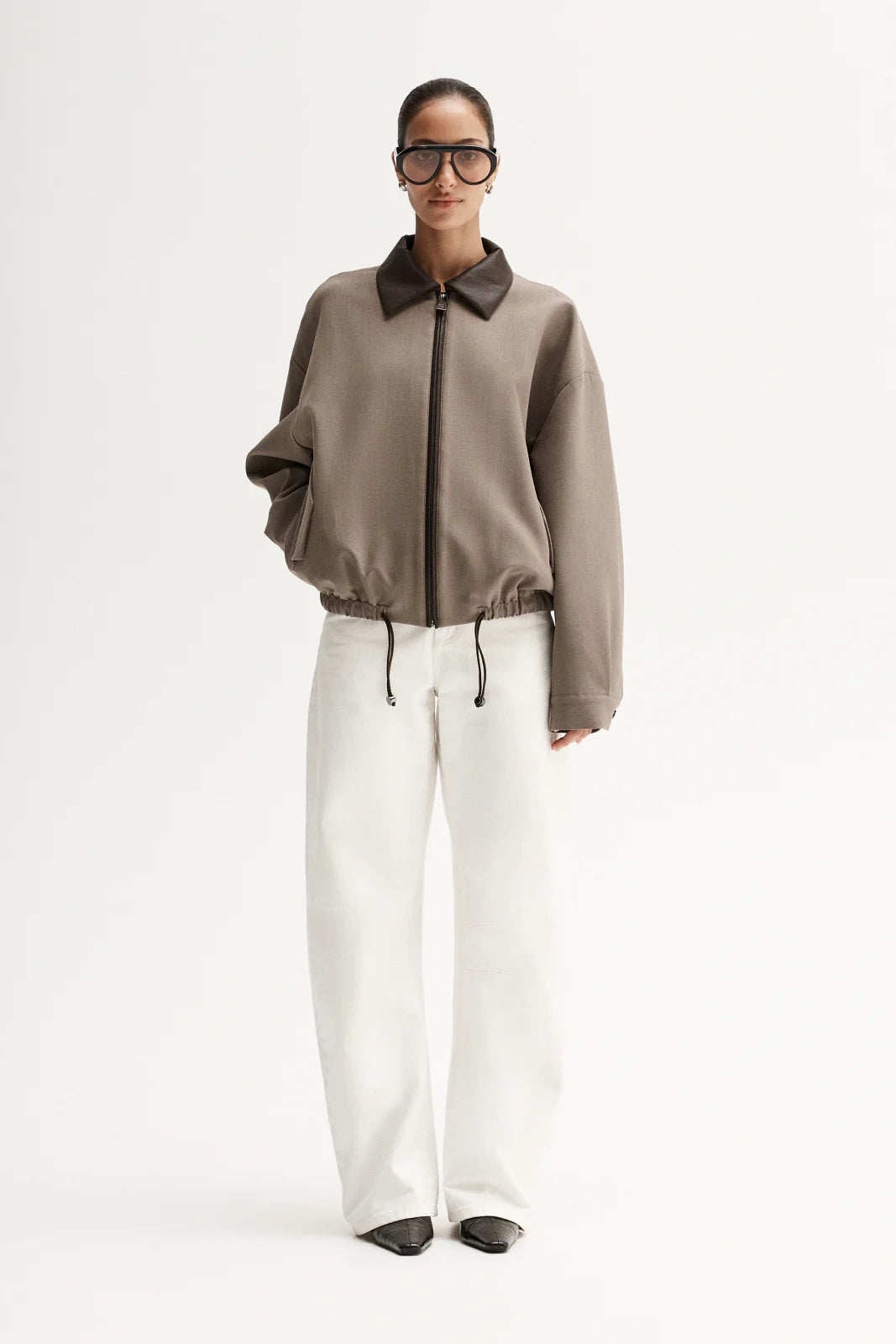 Person wearing a brown jacket with a collar, white pants, and black shoes on a white background