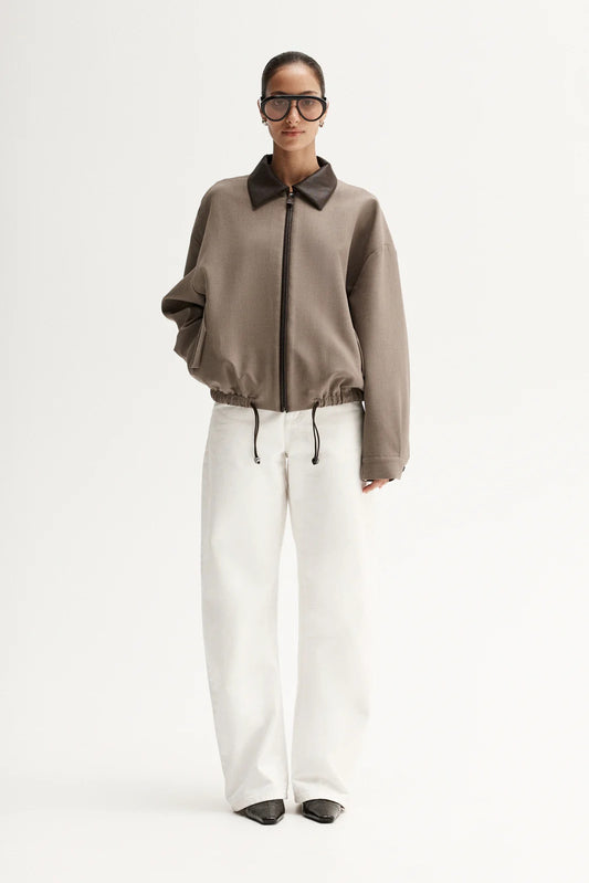 Person wearing a brown jacket with a collar, white pants, and black shoes on a white background