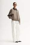 Person wearing a brown jacket and white pants on a white background