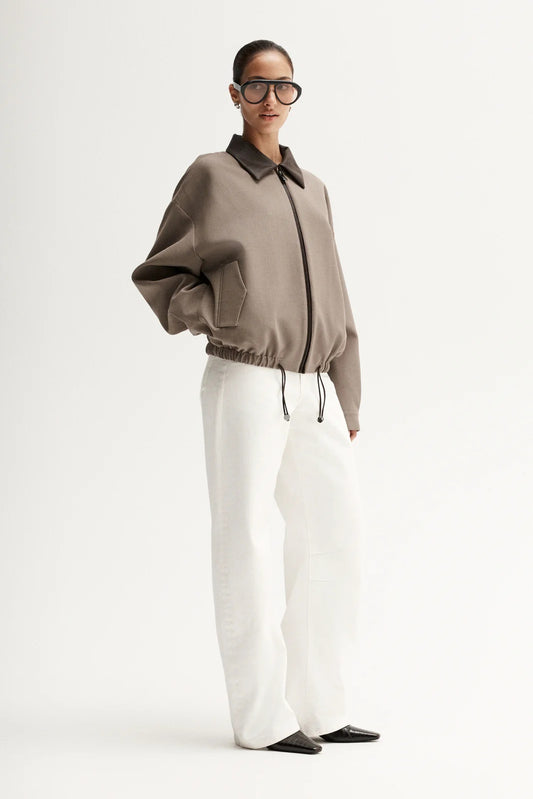 Person wearing a brown jacket and white pants on a white background