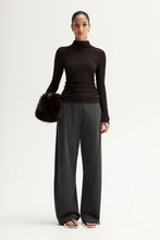 Woman wearing a black turtleneck and gray pants on a white background