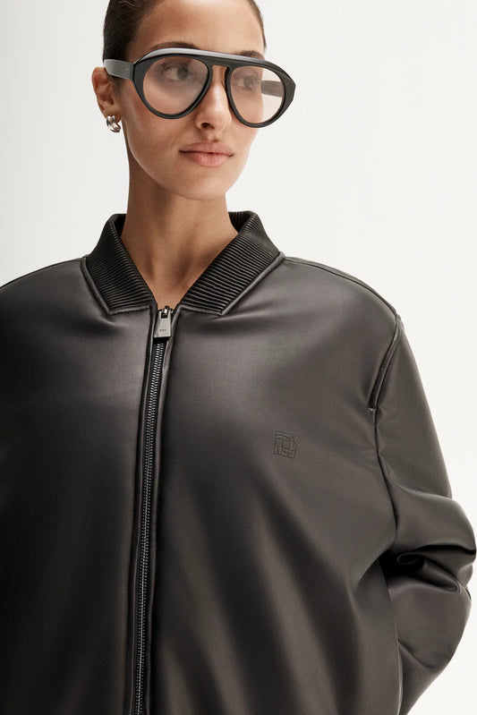 Person wearing a dark gray bomber jacket with a brand logo on a light gray background