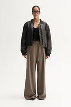 Person wearing a black bomber jacket and beige pants on a white background