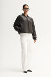 Person wearing a dark gray bomber jacket and white pants on a white background
