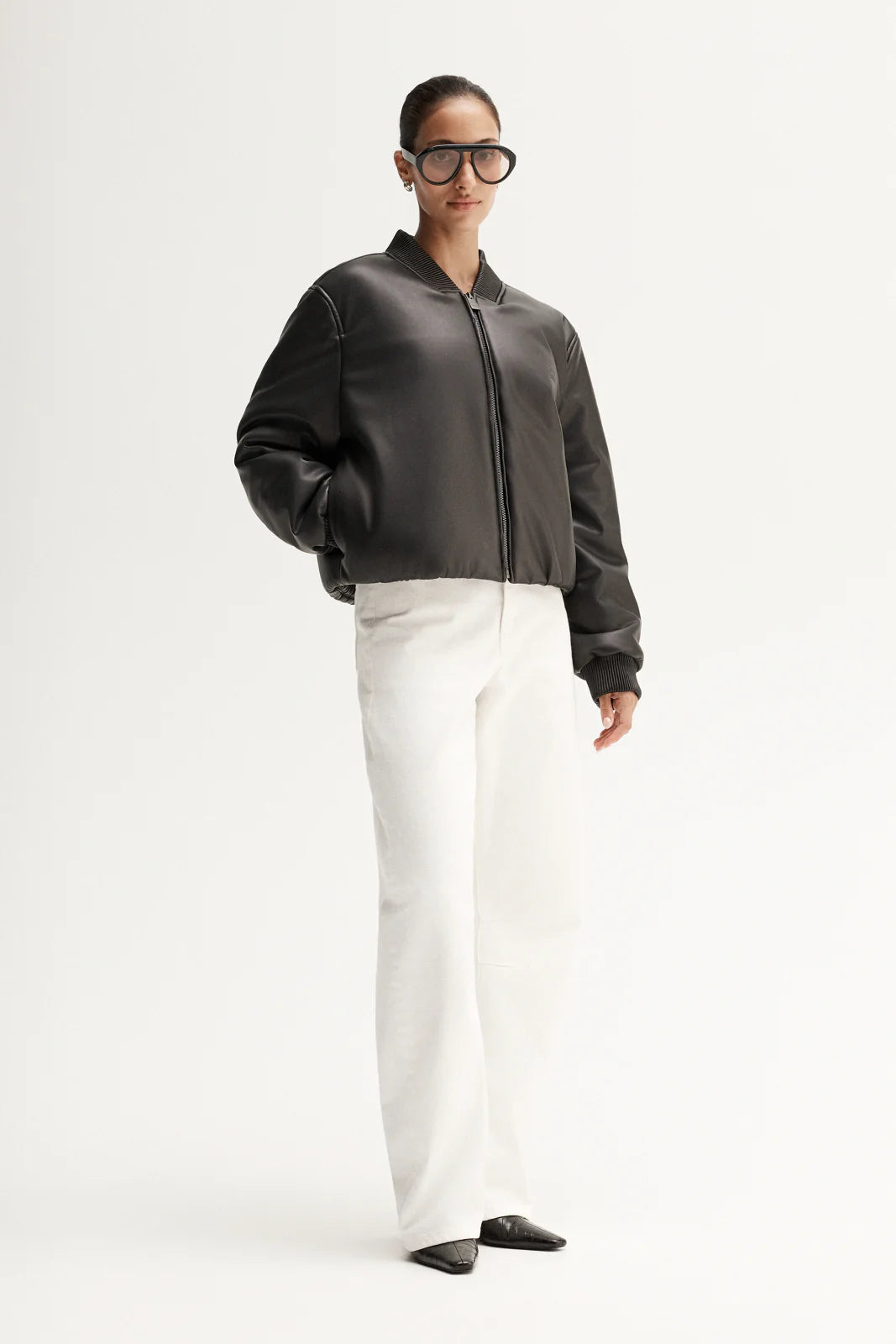 Person wearing a dark gray bomber jacket and white pants on a white background