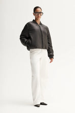 Person wearing a dark gray bomber jacket and white pants on a white background