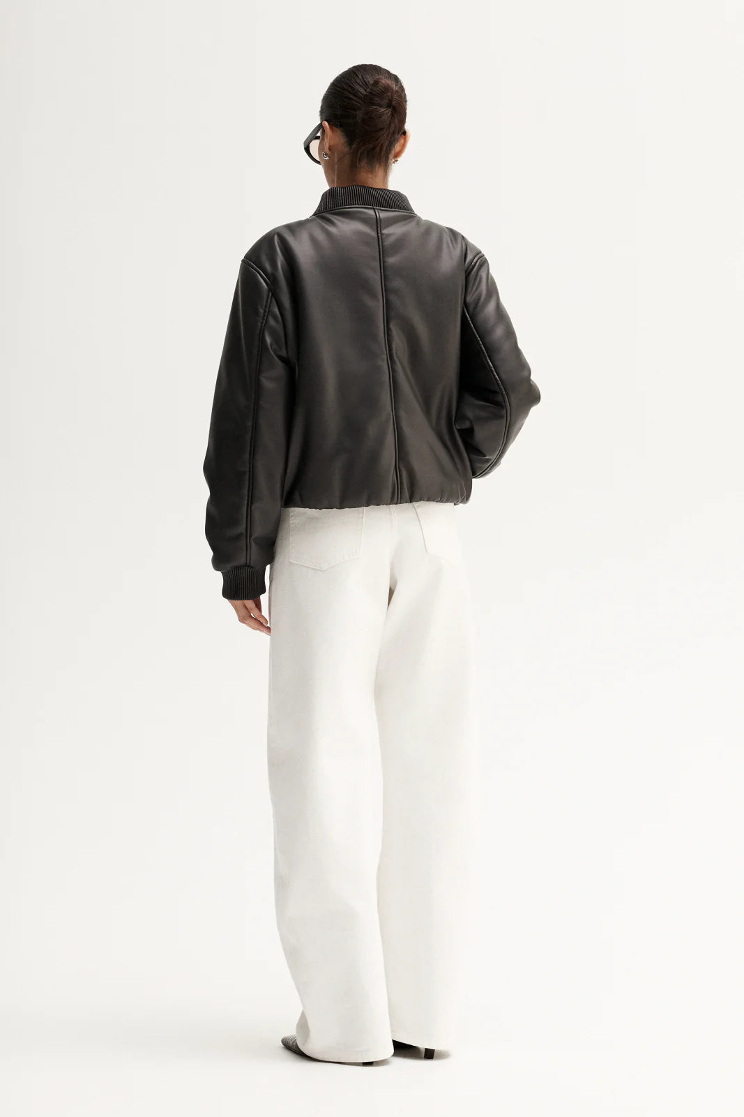 Model wearing the jacket with white wide-leg trousers, back angled view
