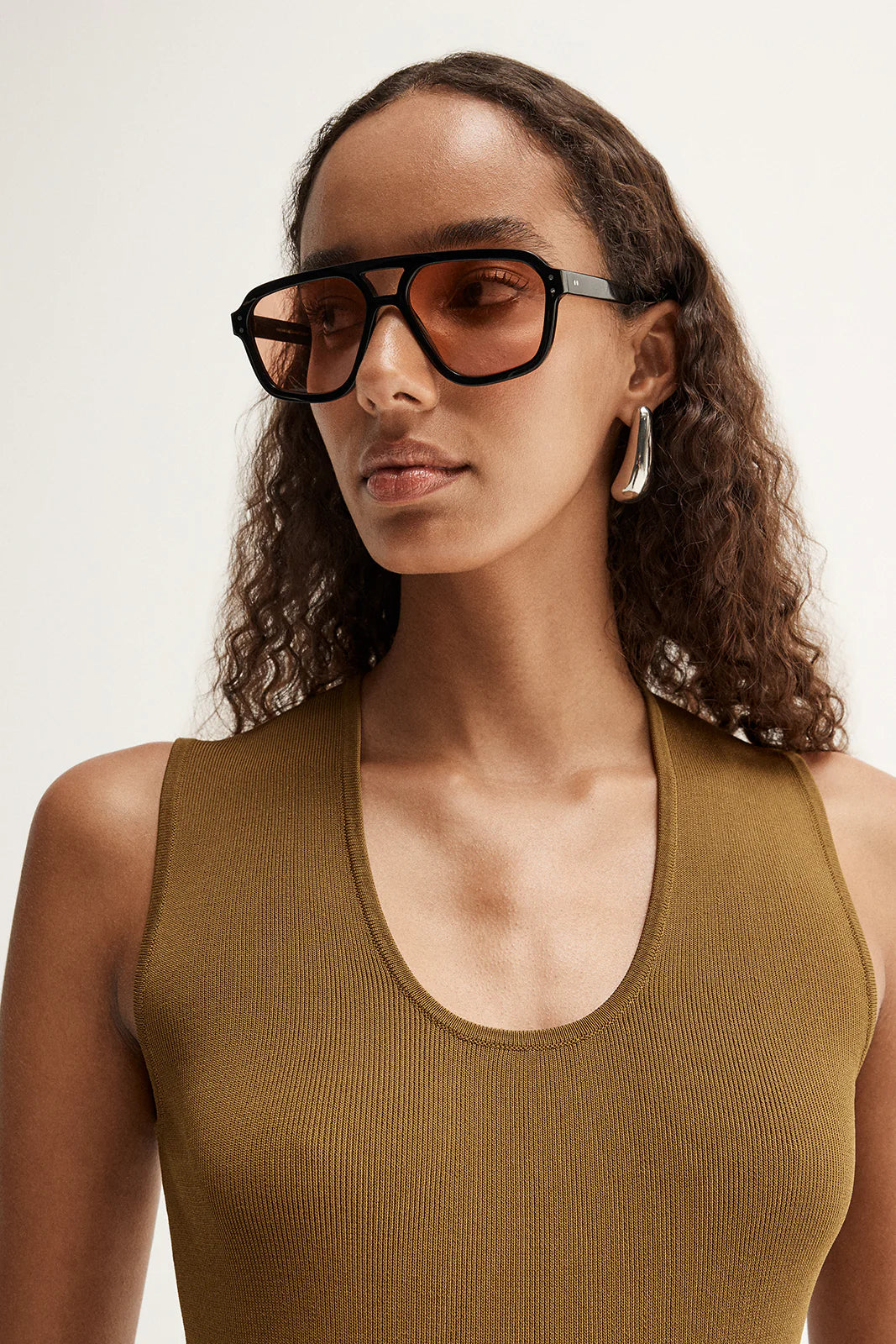 Close-up of model wearing the moss Hayes Knit with sunglasses, showing the narrow scoop neckline, wide shoulder straps and fine ribbed texture, front view
